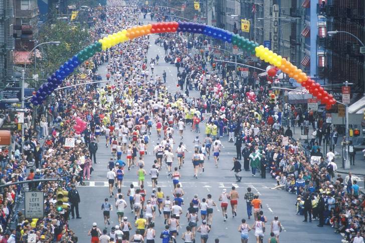 A crowd of runners under a rainbow arc made of balloons